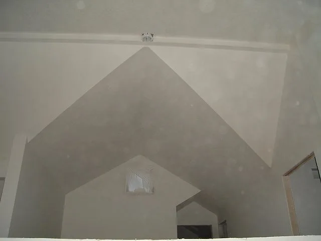 Textured gable wall and angled ceiling planes primed white, with a small vent near the peak of the vault