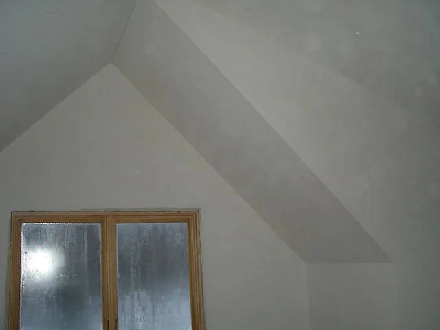 Vaulted ceiling and gable wall with fresh knockdown-style texture, above a window frosted over in winter