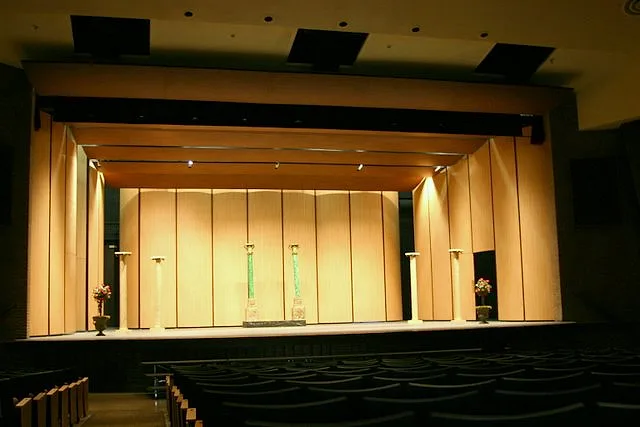 Fregeau Auditorium stage with warm wood panel walls and lighting, seen from the seats under the stepped ceiling