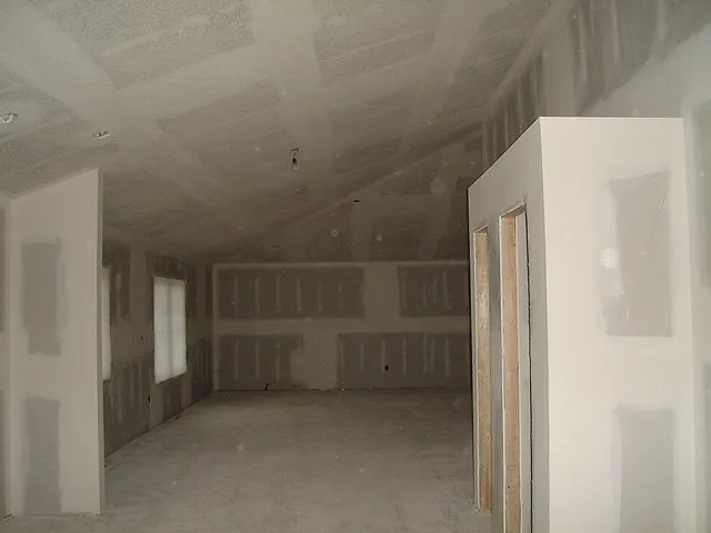 Long addition with freshly hung and taped drywall on walls and a sloped ceiling, door openings framed on the right
