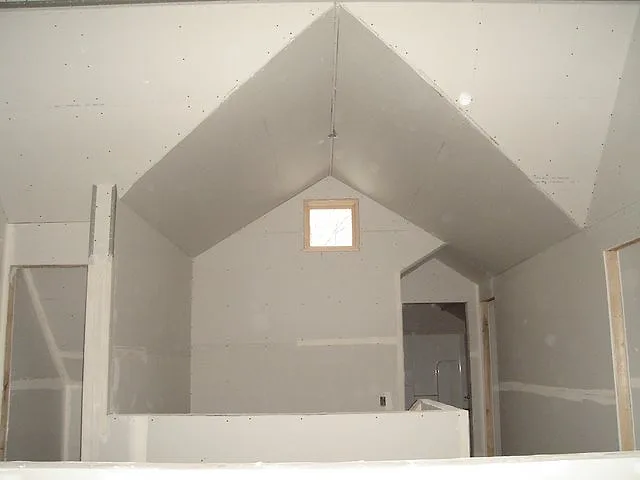 Loft with a steep gable wall in finished drywall, a small window high in the peak and a half-wall railing