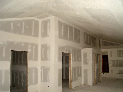 New-construction hallway with taped and mudded drywall corners, door openings and a sloped ceiling above