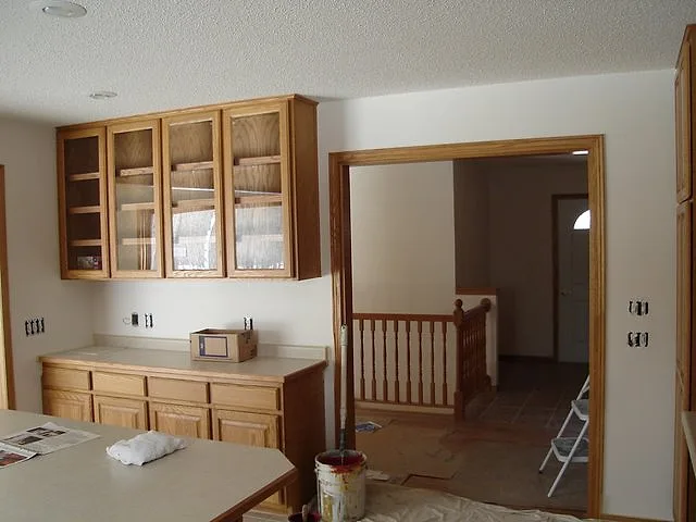 Kitchen with oak cabinets and fresh white walls, a paint can and stepladder still in the room during a new-home paint job