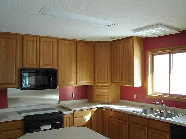 Painted kitchen corner with oak cabinets, a black range and a red accent wall below a textured white ceiling
